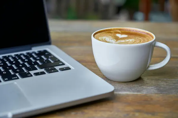 Laptop on a wooden table in a sunlit San Cristóbal café with cortado and notebook
